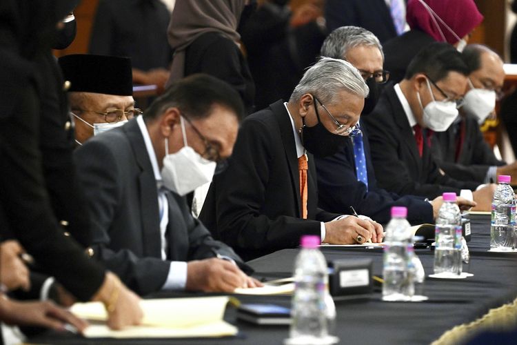 Foto dari Kementerian Informasi Malaysia menunjukkan Perdana Menteri Ismail Sabri Yaakob (tengah) dan pemimpin oposisi Anwar Ibrahim (kiri) menandatangani dokumen kerja sama di gedung parlemen, Kuala Lumpur, Senin (13/9/2021).