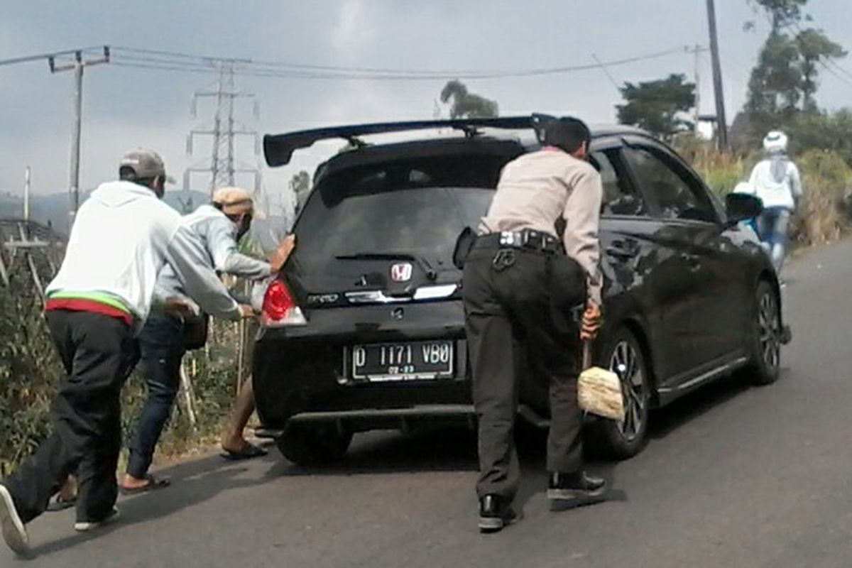 Tampak petugas dan warga tengah membantu mendorong serta mengganjal kendaraan pemudik yang mogok di jalur tanjakan Kamojang-Ibun.