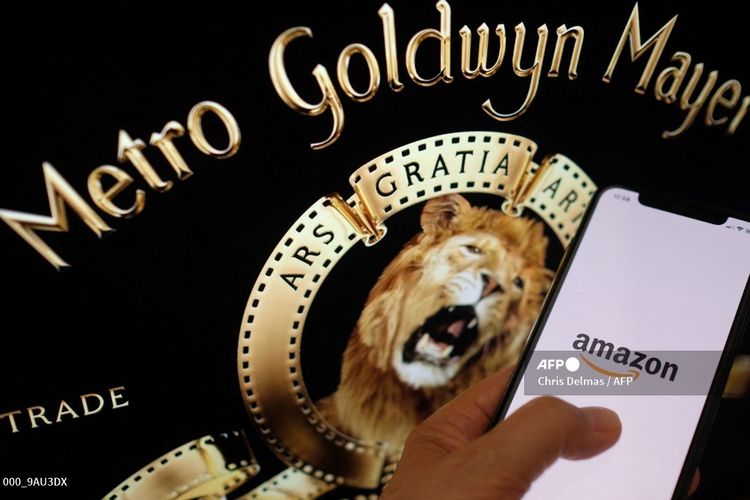 Foto ilustrasi yang diambil pada 26 Mei 2021 ini menunjukkan logo Amazon di ponsel di depan logo MGM di layar komputer di Los Angeles. Amazon mengakuisisi MGM studios dengan nilai Rp 120 triliun.