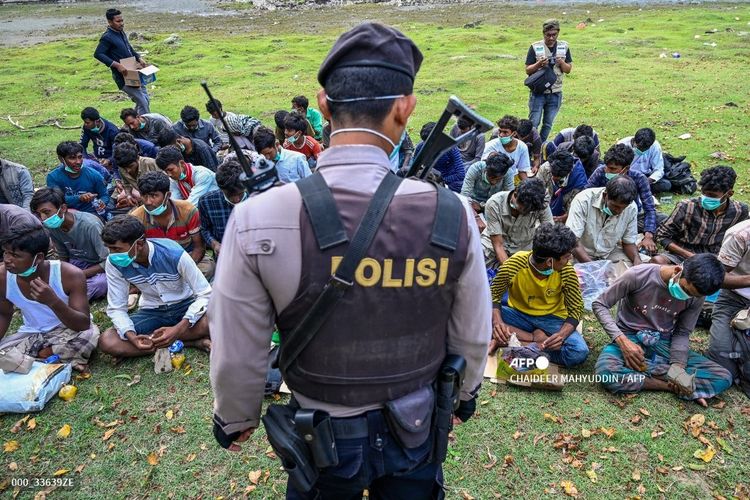 Polisi berjaga di samping pengungsi Rohingya yang menunggu untuk dipindahkan ke tempat penampungan sementara setelah kedatangan mereka dengan perahu di Krueng Raya, provinsi Aceh pada 25 Desember 2022.