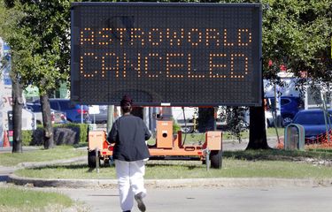 Pejalan kaki melintasi Main Street di depan papan pengumuman pembatalan Astroworld pada Sabtu, 6 November 2021, di Houston. 