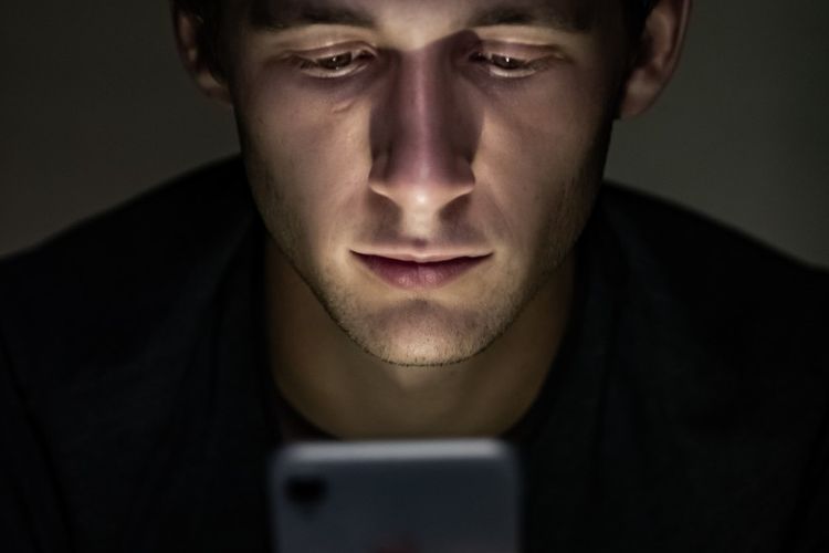 Ilustrasi pengguna sedang menatap ponselnya di suasana gelap.