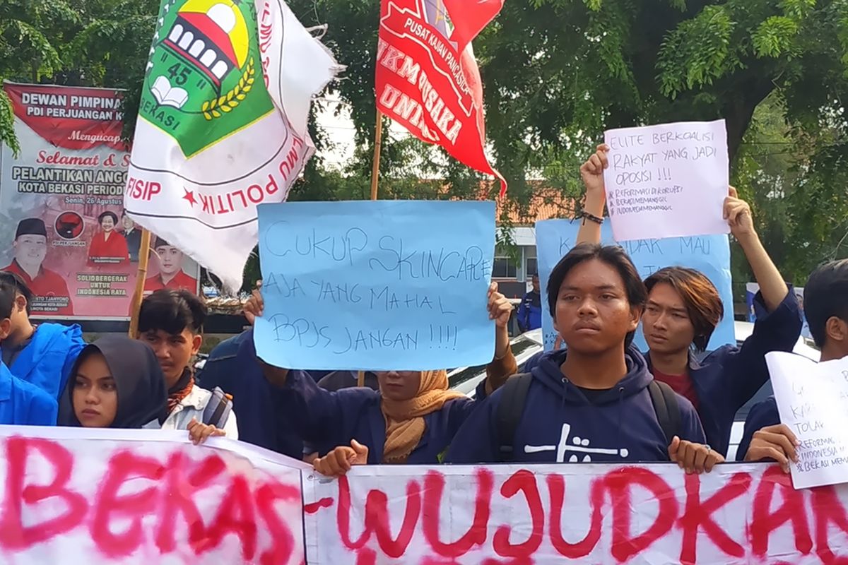 Seorang mahasiswi Front Mahasiswa Bekasi mengacungkan pesan tuntutan agar pemerintah urung menaikkan iuran BPJS Kesehatan dalam aksi unjuk rasa di depan gedung DPRD Kota Bekasi, Senin (28/10/2019).