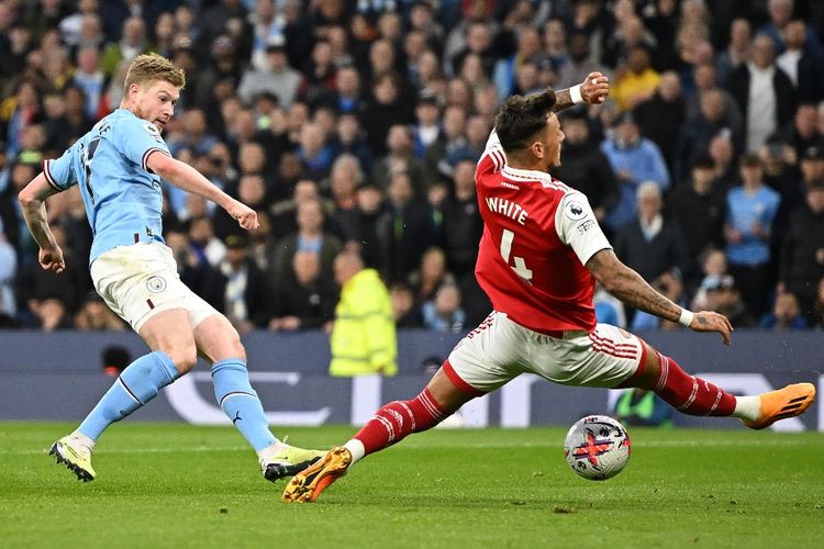 Bek Arsenal, Ben White (kanan), coba melakukan blok terhadap tembakan gelandang Manchester City, Kevin De Bruyne, dalam pertandingan pekan ke-33 Liga Inggris 2022-2023 yang digelar di Stadon Etihad pada Rabu (26/4/2023) malam waktu setempat. Artikel ini berisi link live streaming Arsenal vs Man City di Community Shield 2023. (Foto oleh OLI SCARFF/AFP)