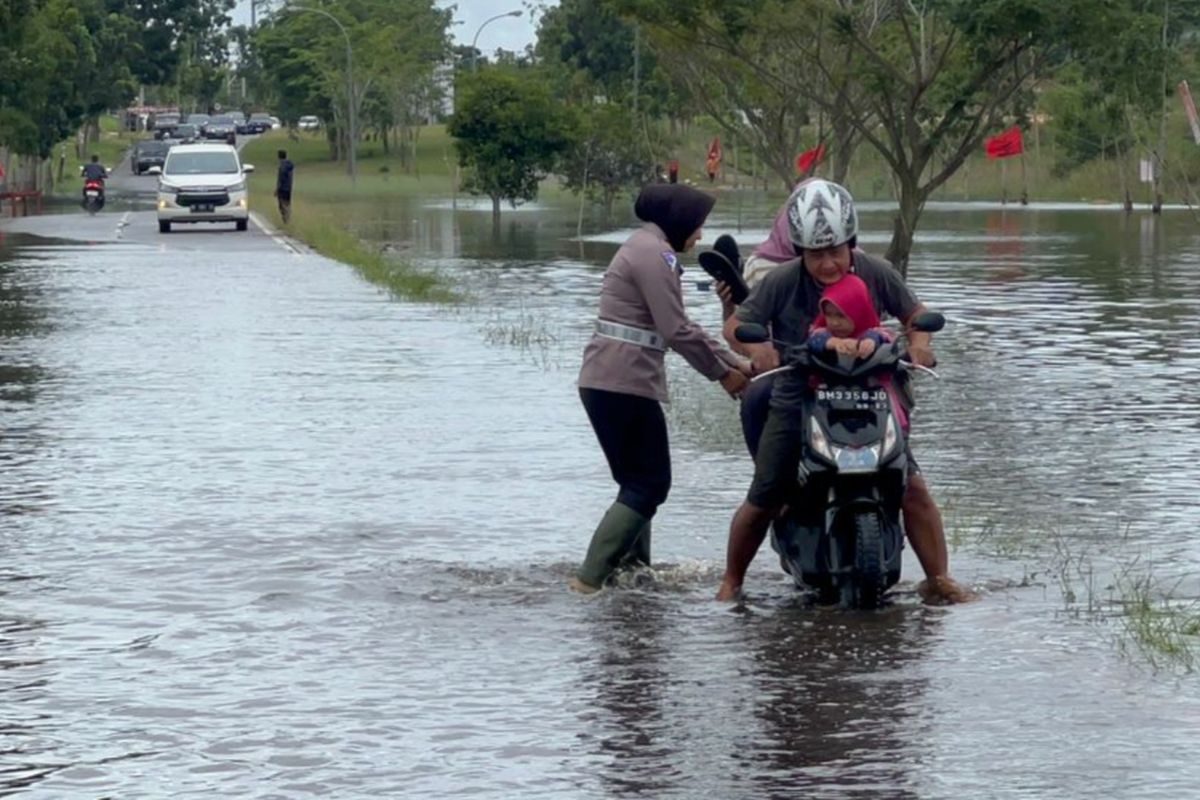 Kasatlantas Polres Pelalawan, AKP Akira Ceria mendorong motor warga yang mogok saat melewati jalan yang banjir, di Kecamatan Pangkalan Kerinci, Kabupaten Pelalawan, Riau, Rabu (27/12/2023).