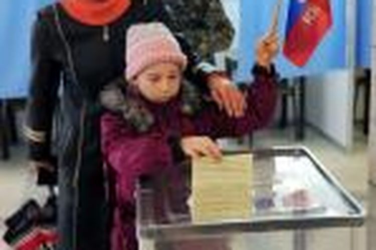 Seorang anak memasukkan surat suara ibunya sambil memegang bendera Rusia pada referendum di Simferopol, Crimea, Ukraina, Minggu (16/3/2014). 

