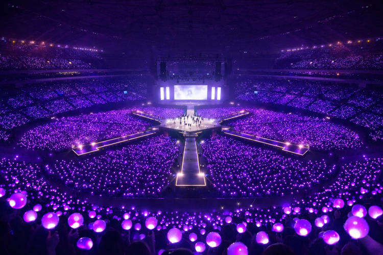 Ilustrasi suasana konser comeback BTS 2026 dengan panggung 360 derajat dan dikelilingi purple ocean.