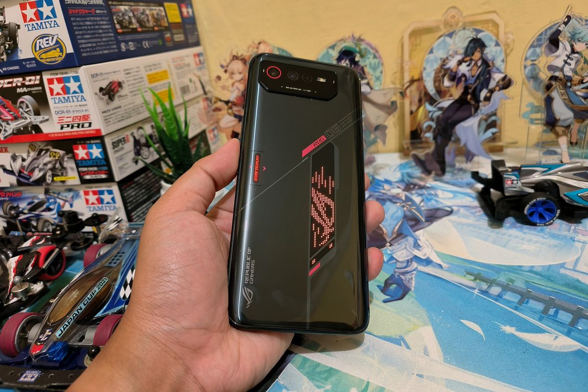 Bagian punggung Asus ROG Phone 6. Logo ROG yang bisa menyala kini seakan dimuat dalam sebuah bidang yang menyerupai jajar genjang. Pada ROG Phone 5, logo ROG terkesan hanya ditempelkan begitu saja di punggung perangkat.

Selain logo ROG, punggung ROG Phone 6 juga kini dibekali dengan tulisan Dare to Play yang bisa menyala.

Untuk menemani dua logo yang menyala tersebut, Asus juga menyematkan beberapa garis simetri, serta tulisan dan logo ROG lainnya untuk membuat cangkang ponsel gaming ini cantik.

Lalu, ada pula modul menonjol dengan bentuk mirip bidang trapesium, yang memuat tiga kamera, terdiri dari kamera utama 50 MP, kamera ultrawide 13 MP, dan kamera makro 5 MP.