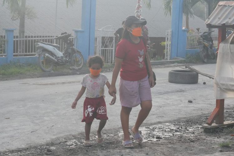 Seorang ibu dan anak mengenakan masker untuk melindungi diri dari abu vulkanis letusan Gunung Lewotobi Laki-laki di Flores Timur, NTT, Selasa (2/1/2024). Kompas.com/Serafinus Sandi