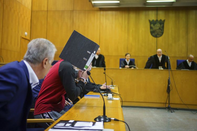 Dengan folder file di depan wajahnya, Taha Al-Jumailly (2 dari kiri) duduk di dok sebelum vonis dijatuhkan di Pengadilan Tinggi Regional Frankfurt di Frankfurt, Jerman, Selasa, 30 November 2021. 