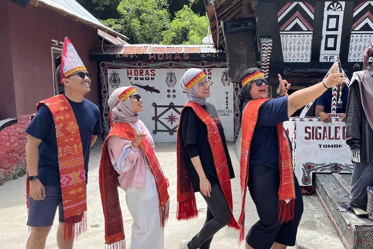 Wisatawan memakai ulos dan sortali sebelum ikut manortor di Sigale-gale, Desa Tomok, Kabupaten Samosir, Sumatera Utara, Jumat (16/5/2025). 