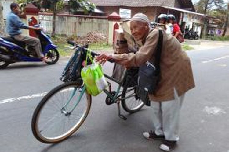 Atmo Tohari atau Mbah Tohari berjalan menuntut sepeda untuk menjajakan dagangannya berupa sabun dan kebutuhan rumah tangga lainnya, di jalan kawasan Desa Bulurejo. Kecamatan Mertoyudan Kabupaten Magelang, Jawa Tengah.