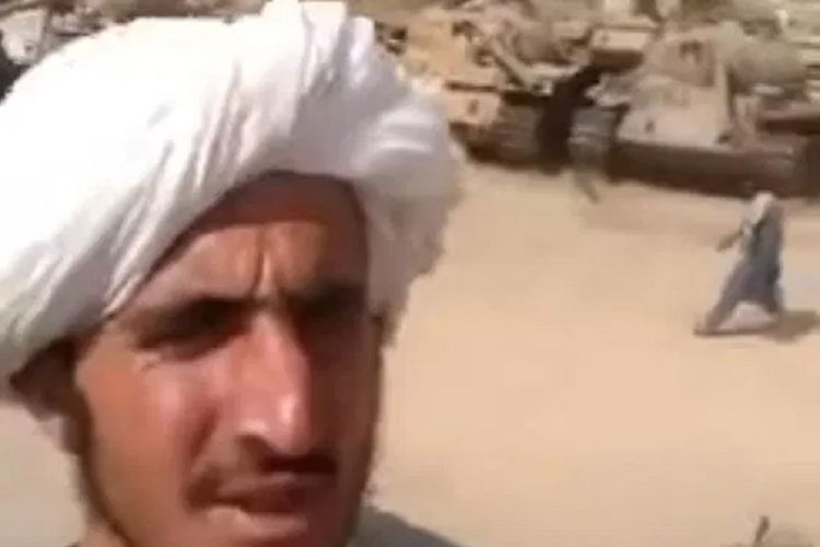 Dalam tangkapan video, seorang anggota Taliban berpose dengan latar belakang tank yang mereka sita dari pasukan AS.