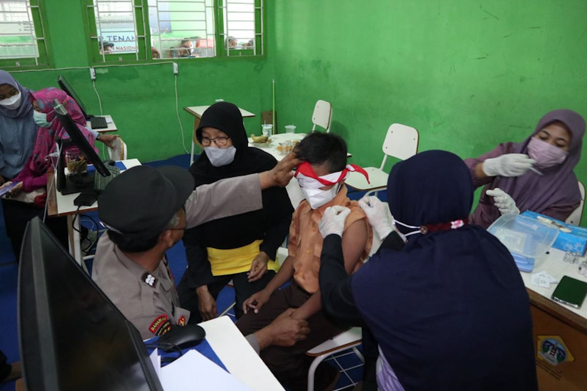 Bintang Al Qhiromi Pratama Putra alias Kiki (tengah) saat menjalani agenda vaksinasi di SD Negeri 39 Gresik dengan mata ditutup hasduk, Jumat (21/1/2022).