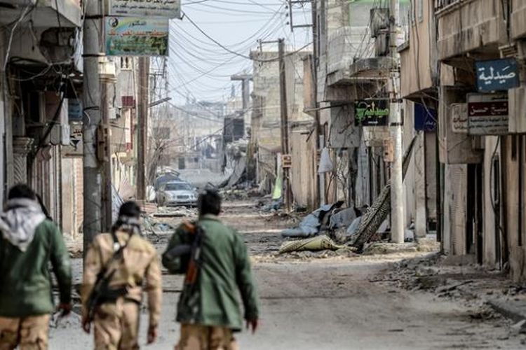 Beberapa pejuang Kurdi Suriah berjalan di salah satu sudut kota Kobani yang hancur lebur akibat pertempuran. Setelah empat bulan pertumpahan darah yang brutal, pejuang Kurdi yang dibantu serangan udara koalisi internasional berhasil memukul mundur pasukan ISIS.