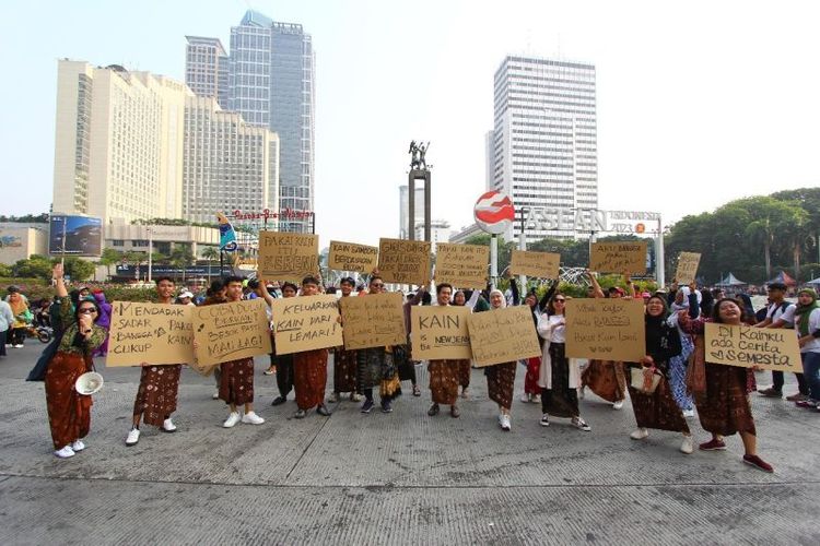 Sejumlah orang membentangkan poster berisi ajakan menggunakan produk lokal dan fesyen ramah lingkungan dalam kegiatan Parade Berkain Lokal Lestari, di kawasan Bundaran Hotel Indonesia, Jakarta, Minggu (8/10/2023).