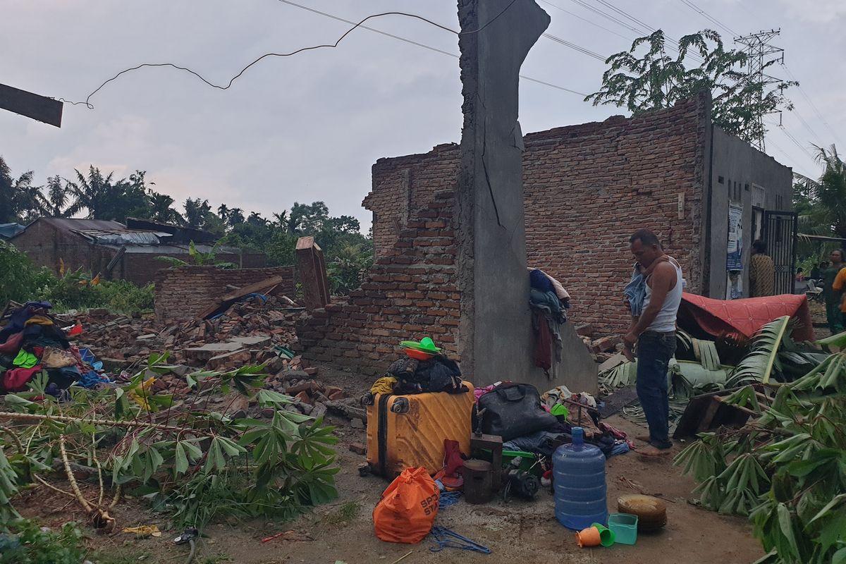 Maruli Manurung (47) sedang menggendong anaknya di depan rumahnya yang roboh karena diterjang angin kencang di Desa Amplas, Kecamatan Percut Sei Tuan, Kabupaten Deli Serdang pada Jumat (23/5/2025). 
