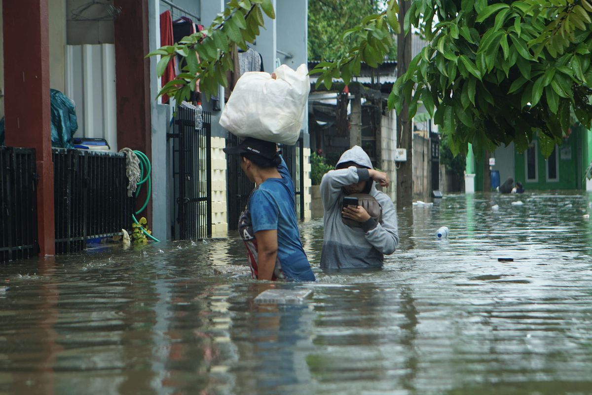 Warga melintasi genangan banjir di kawasan Perumahan Karang Satria 2 Green Residence, Bekasi Timur, Kota Bekasi, Minggu (18/1/2026). Banjir berulang di Jawa Barat dan Jabodetabek dinilai tak cukup diatasi dengan aksi viral. Ini pentingnya regulasi tata ruang untuk mitigasi bencana.