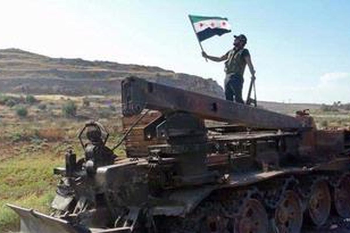 Seorang anggota Tentara Pembebasan Suriah (FSA) mengibarkan Suriah pra-Baath di atas kendaraan militer pemerintah yang dioleh para aktivis dihancurkan oleh FSA, di Binnish, Idlid, Selasa (10/7/2012). 