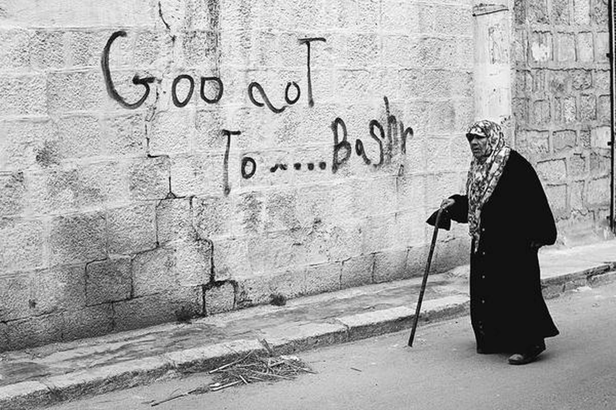 Seorang perempuan berjalan di depan tulisan dalam bahasa Inggris yang maksudnya adalah Keluarlah Bashar (