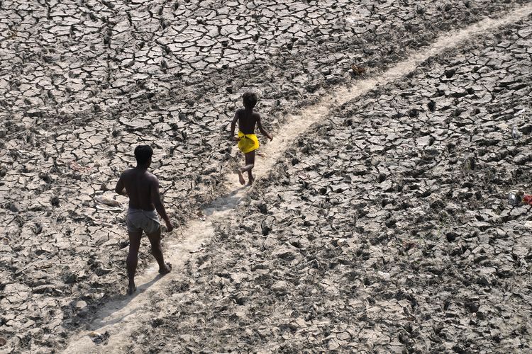 Seorang pria dan anak laki-laki berjalan di sungai Yamuna yang hampir kering total akibat cuaca panas di New Delhi, India, 2 Mei 2022.