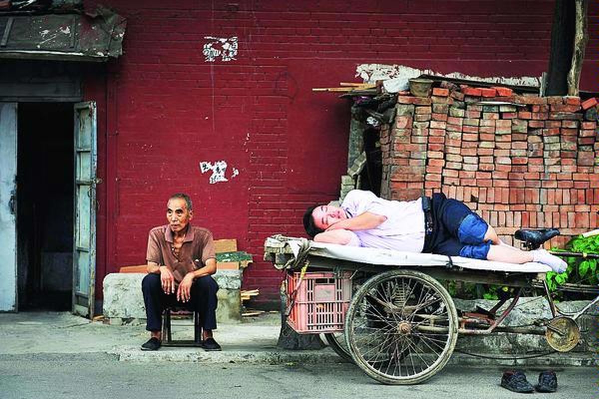 Seorang tua duduk di samping seorang lelaki yang tidur di atas sebuah kendaraan roda tiga di Beijing, China, Rabu (18/8) lalu. Pemerintah China, Selasa, menyatakan, negerinya masihlah sebuah negara berkembang meskipun kini menjadi negara ekonomi nomor dua dunia. Pernyataan itu menunjukkan keengganan China untuk mengambil alih kewajiban baru berkaitan dengan perubahan iklim dan isu lingkungan lainnya.