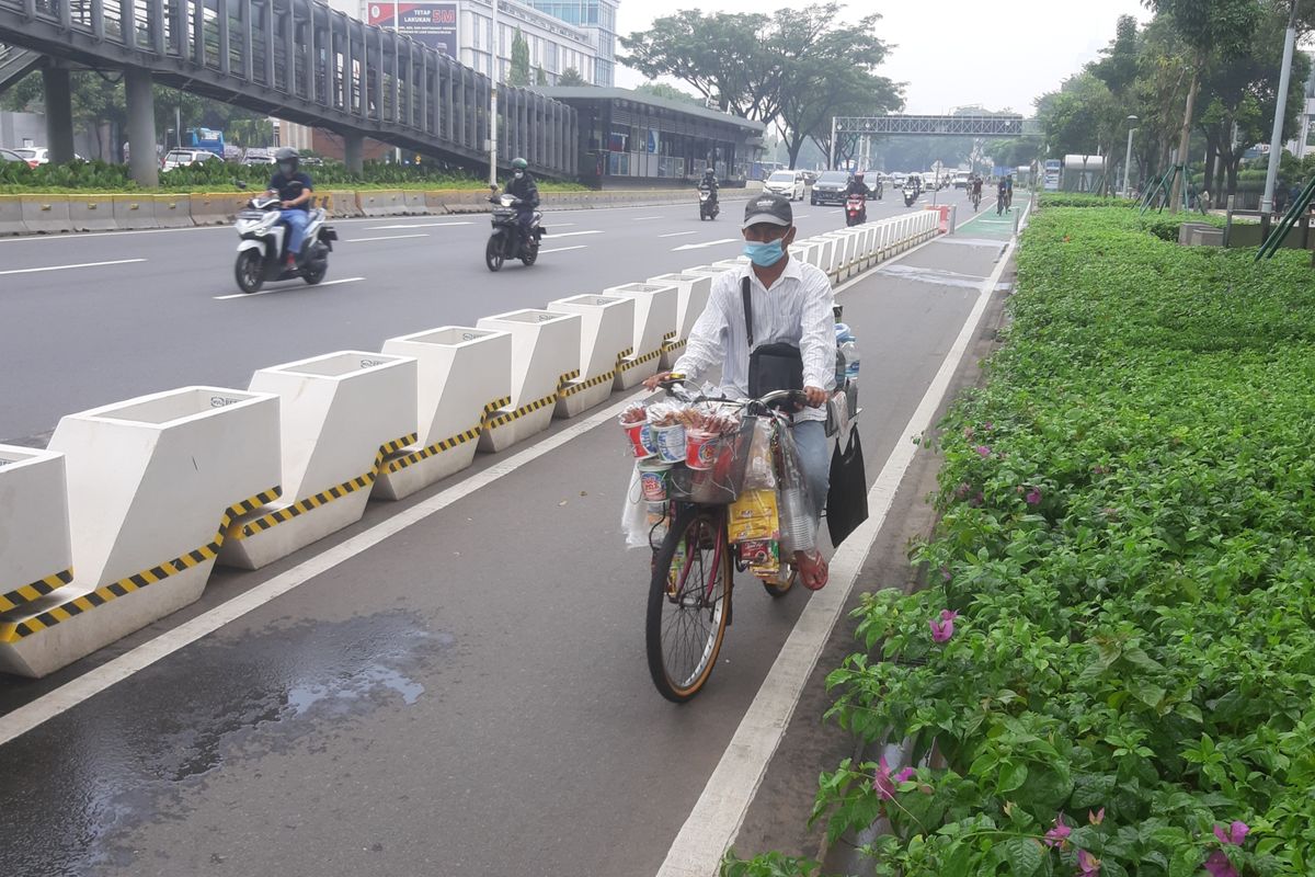 Zaini, salah seorang penjual kopi keliling saat melintas di jalur sepeda terproteksi di Jalan Sudirman, Jakarta, Sabtu (29/5/2021).