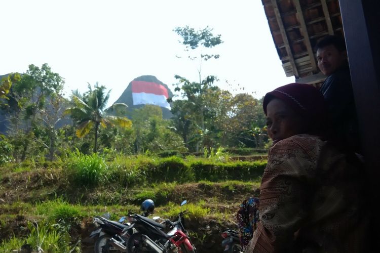 Seorang warga menyaksikan bendera raksasa di Puncak Gunung Buchu, Sekitar Gunung Api Purba Nglanggeran, Patuk, Gunungkidul, DI Yogyakarta, Senin (13/8/2018). 