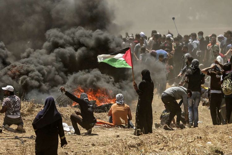 Seorang perempuan warga Palestina memegang bendera negaranya saat terjadi bentrokan dengan pasukan Israel di dekat perbatasan antara jalur Gaza dan Israel, di sebelah timur Kota Gaza, Senin (14/5/2018). Otoritas Palestina menyebut pasukan Israel telah menewaskan 55 orang dan melukai 2.700 orang dalam aksi protes dan bentrokan menentang pembukaan Kedutaan Besar Amerika Serikat di Yerusalem.