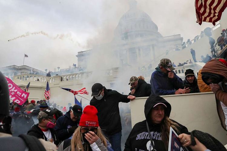 Pendukung Presiden Amerika Serikat Donald Trump menutup wajah mereka dari gas air mata saat bentrok dengan polisi di depan Gedung US Capitol di Washington, Amerika Serikat, Rabu (6/1/2021). Hari pengesahan kemenangan presiden terpilih Joe Biden oleh Kongres di Gedung Capitol diwarnai penyerbuan massa pendukung Donald Trump dalam upaya menggagalkan anggota parlemen dari tugas konstitusional mereka.