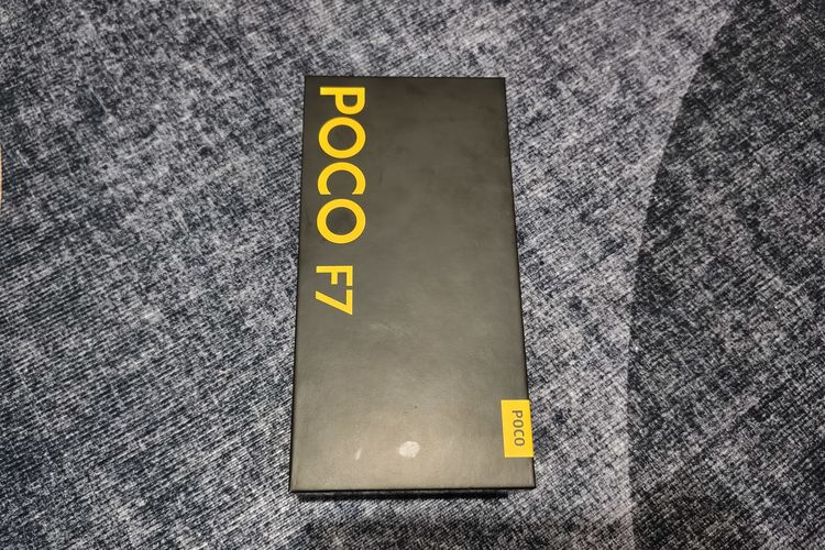 Kotak kemasan Poco F7 tampil dengan dominasi warna hitam dan font kuning khas Poco. Pada bagian depan, terdapat keterangan berupa nama model ponsel tersebut yaitu Poco F7 serta logo Poco di sisi kanan bawah kotak.