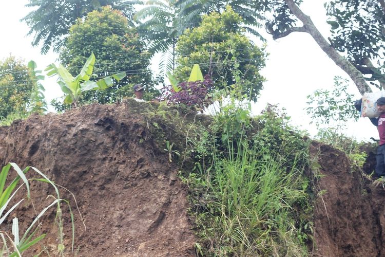 Seorang warga melintasi tebing yang longsor di Kampung Sindanglangu, Desa Batulawang, Kecamatan Cipanas, Kabupaten Cianjur, Jawa Barat akibat pergerakan tanah. 