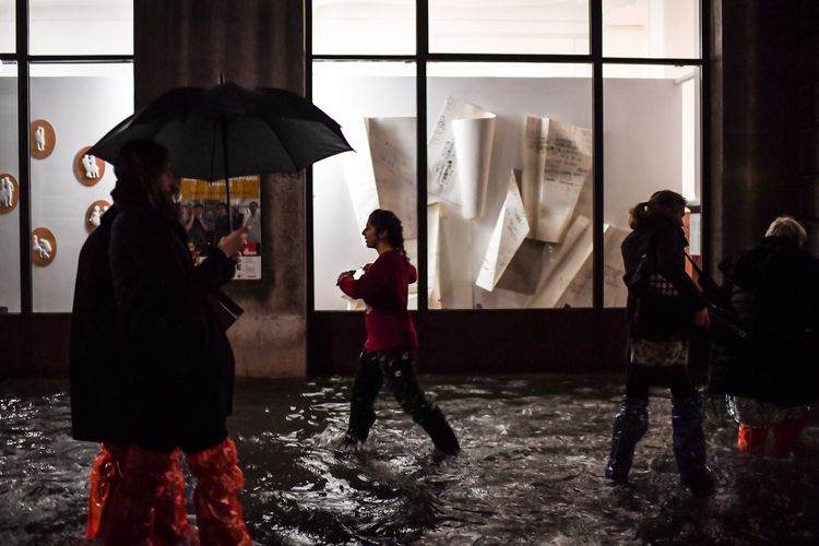 Sejumlah orang berlalu lalang melintasi bangunan di Venesia pada Selasa (12/11/2019). Kota kanal di Italia itu dilanda banjir sebagai akibat gelombang pasang tertinggi dalam 50 tahun terakhir.