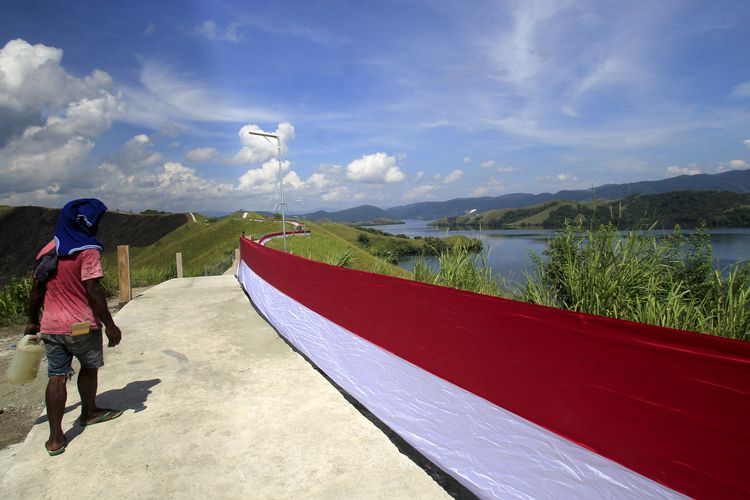 Seorang warga melintasi bendera Merah Putih yang dipasang di bukit Tungku Wiri atau Bukit Teletubies, Kampung Doyo Lama, Distrik Waibu, Kabupaten Jayapura, Papua, Senin (16/8/2021). Pemasangan bendera Merah Putih sepanjang 700 meter tersebut dalam rangka Menyambut HUT ke-76 RI.ANTARA FOTO/Gusti Tanati/wpa.
