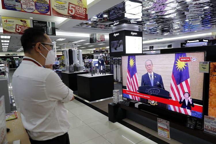 Seorang pegawai toko elektronik mengenakan masker sambil menonton siaran langsung pidato perpisahan Muhyiddin Yassin sebagai Perdana Menteri Malaysia, di Kuala Lumpur, Senin (16/8/2021). Muhyiddin mundur setelah 17 bulan menjabat akibat kehilangan dukungan mayoritas, dan menjadikannya PM Malaysia dengan masa jabatan tersingkat sepanjang masa.