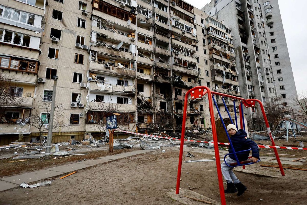 Seorang anak duduk di ayunan di depan gedung tempat tinggal yang hancur, setelah Rusia meluncurkan operasi militer besar terhadap Ukraina, di Kyiv, Ukraina, Jumat (25/2/2022).