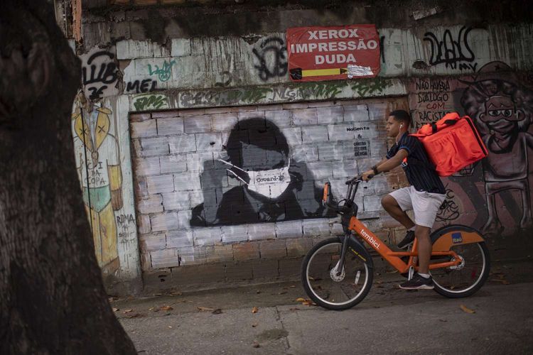 Seorang warga bersepeda melintas di depan gambar mural Presiden Brazil Jair Bolsonaro di Rio de Janeiro, Brazil, 24 Maret 2020. Pandemi Covid-19 yang disebabkan oleh virus corona menjadi insipirasi seniman grafiti untuk memberikan peringatan dan motivasi bagi warga dalam menghadapi virus tersebut.