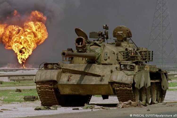 Bangkai sebuah tank Irak dilatari ladang minyak yang dibakar militer dalam invasi Kuwait, 1990.
