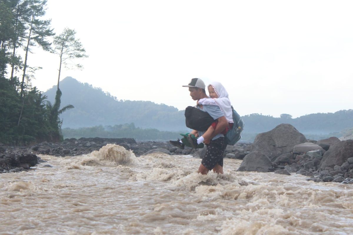 Orang tua siswa di Desa Jugosari menggendong anaknya berangkat ke sekolah menyebrangi aliran lahar Gunung Semeru
