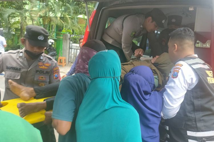 Warga dan polisi membawa masuk Sukarmu ke dalam ambulans, usai pingsan saat turut aksi mendatangi kantor Kejaksaan Negeri Lamongan, Jawa Timur, Senin (6/3/2023).