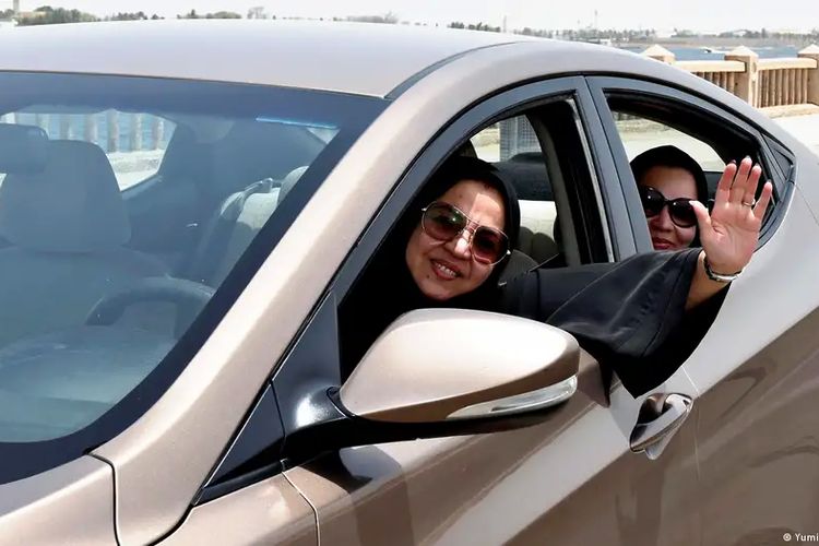 Seorang perempuan sambil tersenyum dan melambaikan tangan saat mengendarai mobil di Jeddah, Arab Saudi.