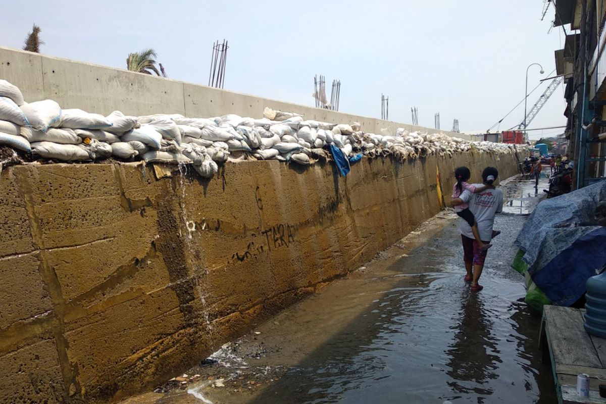 Warga melewati genangan air dari rembesan air laut yang menembus tanggul karung pasir di Muara Baru, Penjaringan, Jakata Utara, Rabu, (3/1/2018)