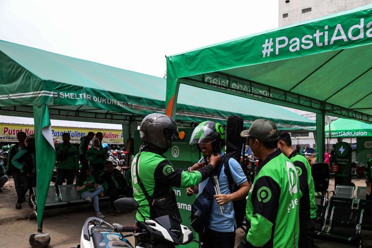 Pengemudi ojek online memakaikan helm kepada penumpangnya di Kawasan Stasiun Sudirman, Jakarat Pusat, Rabu (11/3/2020). Kenaikan tarif ojek online kembali batal.