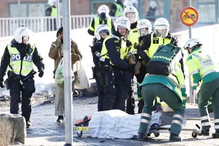 Polisi dan personel ambulans membawa seorang pria terluka yang tertembak di kaki saat kerusuhan di Norrkoping, Swedia pada 17 April 2022.