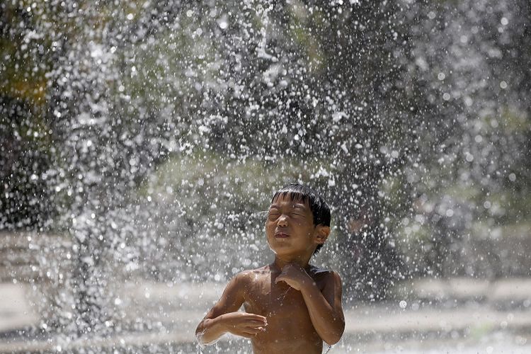 Seorang bocahmendinginkan badan di air mancur saat hari yang panas di sebuah taman di Tokyo, Jepang, pada 5 Agustus 2014. (REUTERS/Toru Hanai)