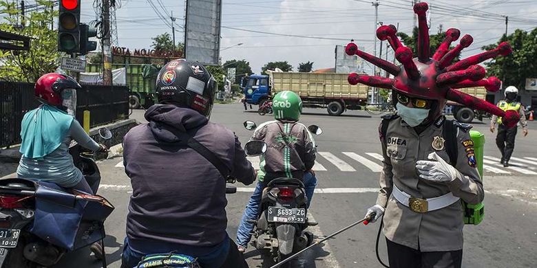 Anggota polisi memakai helm berbentuk virus corona melakukan imbauan dan penyemprotan cairan disinfektan pada kendaraan di jalanan di daerah Mojokerto, Jawa Timur, Jumat (3/4/2020). Cara unik ini dilakukan oleh sejumlah anggota dari Polres Mojokerto dalam upaya menekan penyebaran virus corona atau penyakit Covid-19 yang tengah merebak di Tanah Air.