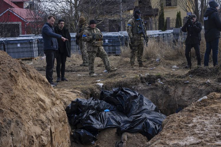 Orang-orang berdiri di samping kuburan massal di Bucha, di pinggiran Kyiv, Ukraina, Senin, 4 April 2022. 