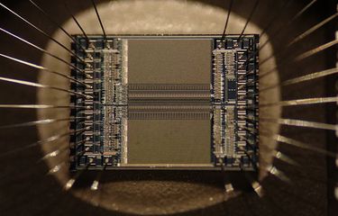 microchip EPROM menunjukkan detail sirkuit terintegrasi itu sendiri dan kabel perak yang menghubungkan die ke kaki chip. Gambar mencakup area sekitar 5 kali 4 mm.