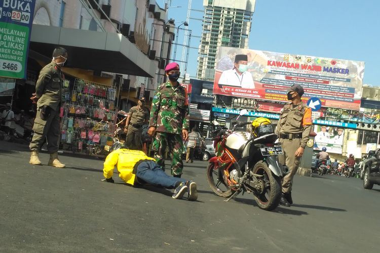 Seorang pengemudi ojek online dihukum push up lantaran tidak mengenakan masker, Selasa (2/6/2020) di Pasar Tengah, Bandar Lampung. Sejumlah warga ditegur aparat kepergok tidak mengenakan masker saat beraktivitas di ruang publik.