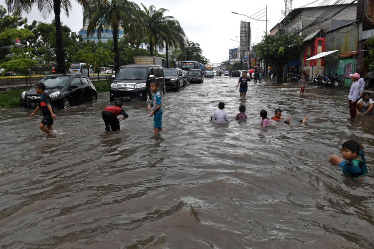 Sejumlah anak bermain air yang membanjiri Jalan Gunung Sahari di Pademangan, Jakarta, Jumat (24/1/2020). Hujan yang mengguyur sejak Jumat pagi hingga siang hari tersebut memicu banjir setinggi 30-50 centimeter di jalan raya itu sehingga menyebabkan lalu lintas kendaraan bermotor dan roda perekonomian warga setempat tersendat.